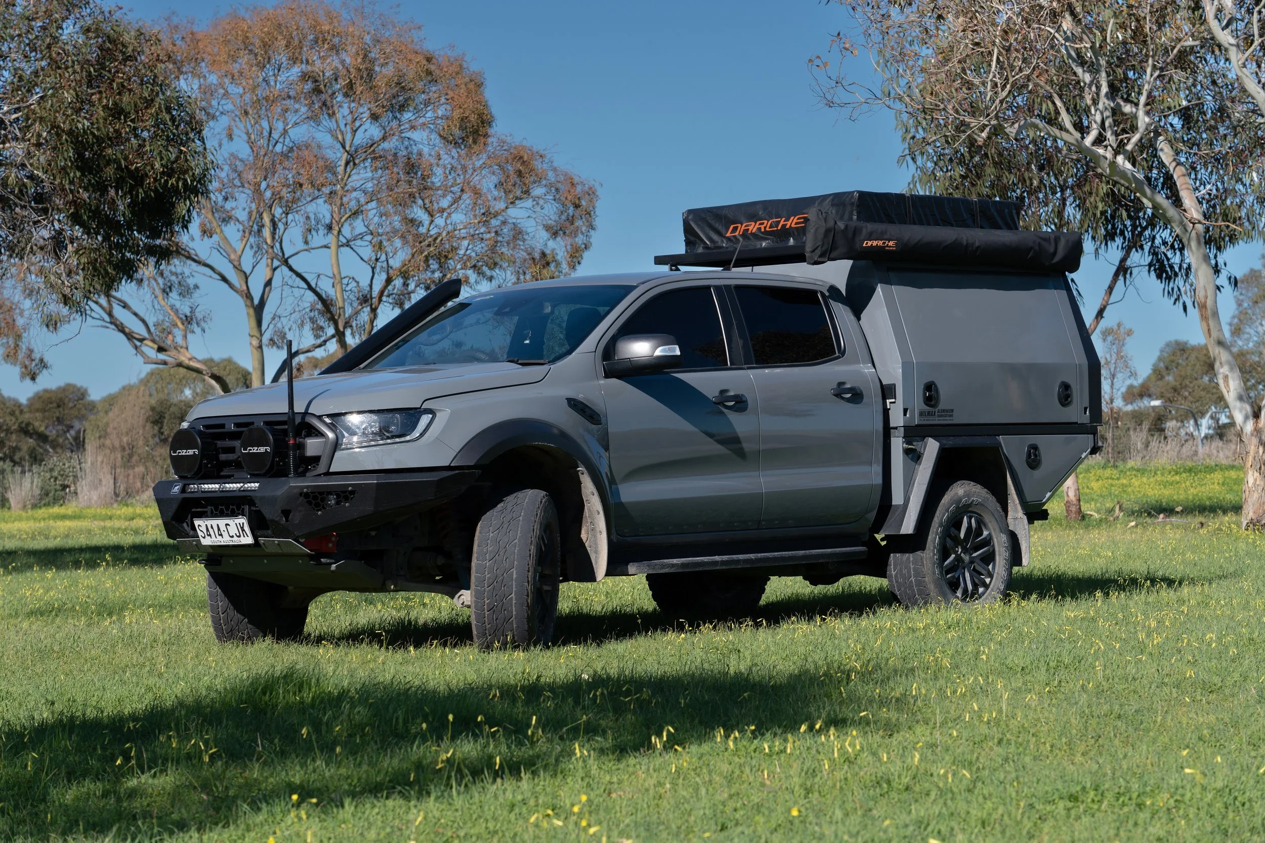 A gray pickup truck with off-road accessories parked on a grassy field with trees and blue sky in the background.