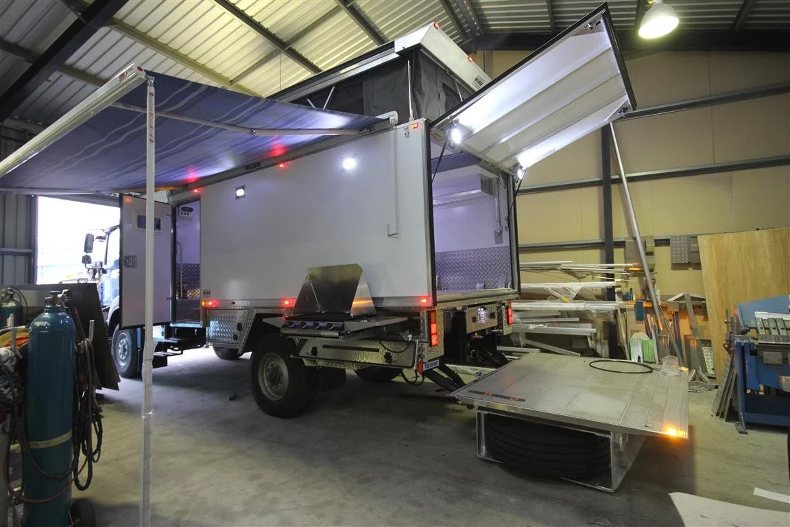 Mobile food truck inside a warehouse with equipment and tools visible around it.