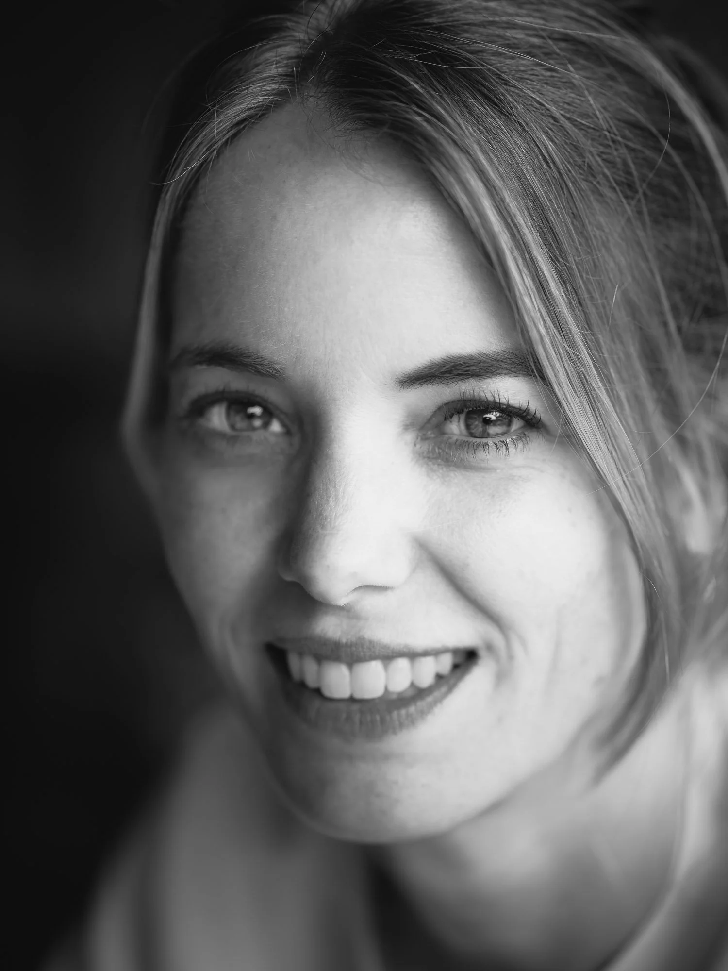 Black and white close-up portrait of a young woman smiling with visible teeth, light-colored hair, and bright eyes.