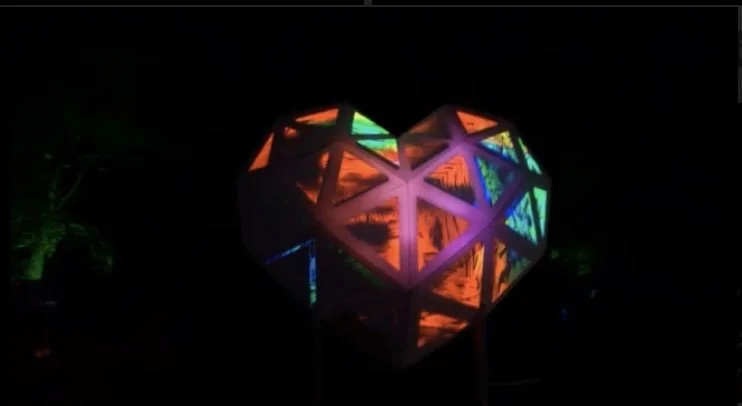 A heart-shaped lantern with colorful LED lights illuminating geometric patterns in a dark setting.