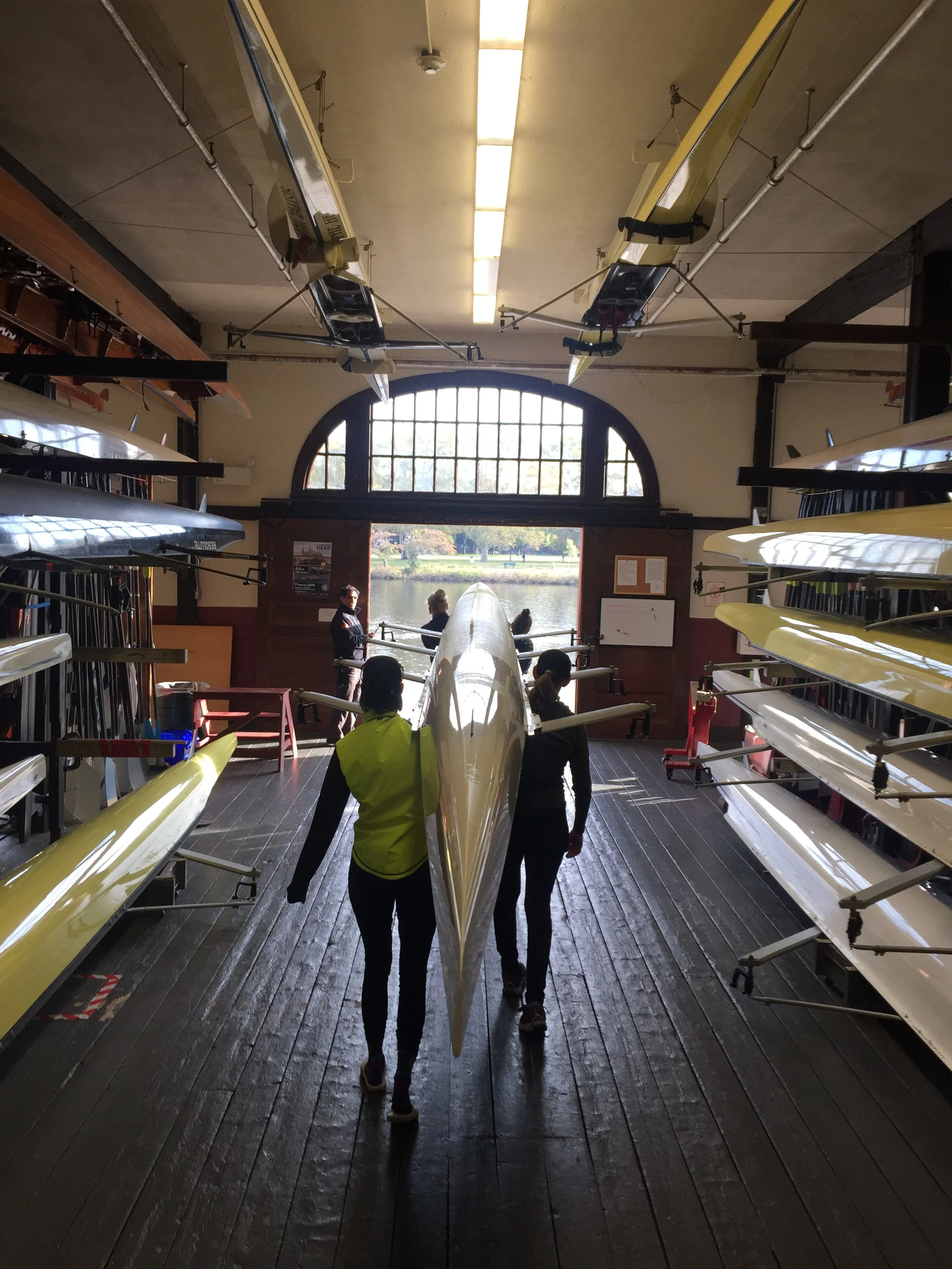 Women carrying quad out of Harvard boathouse to dock