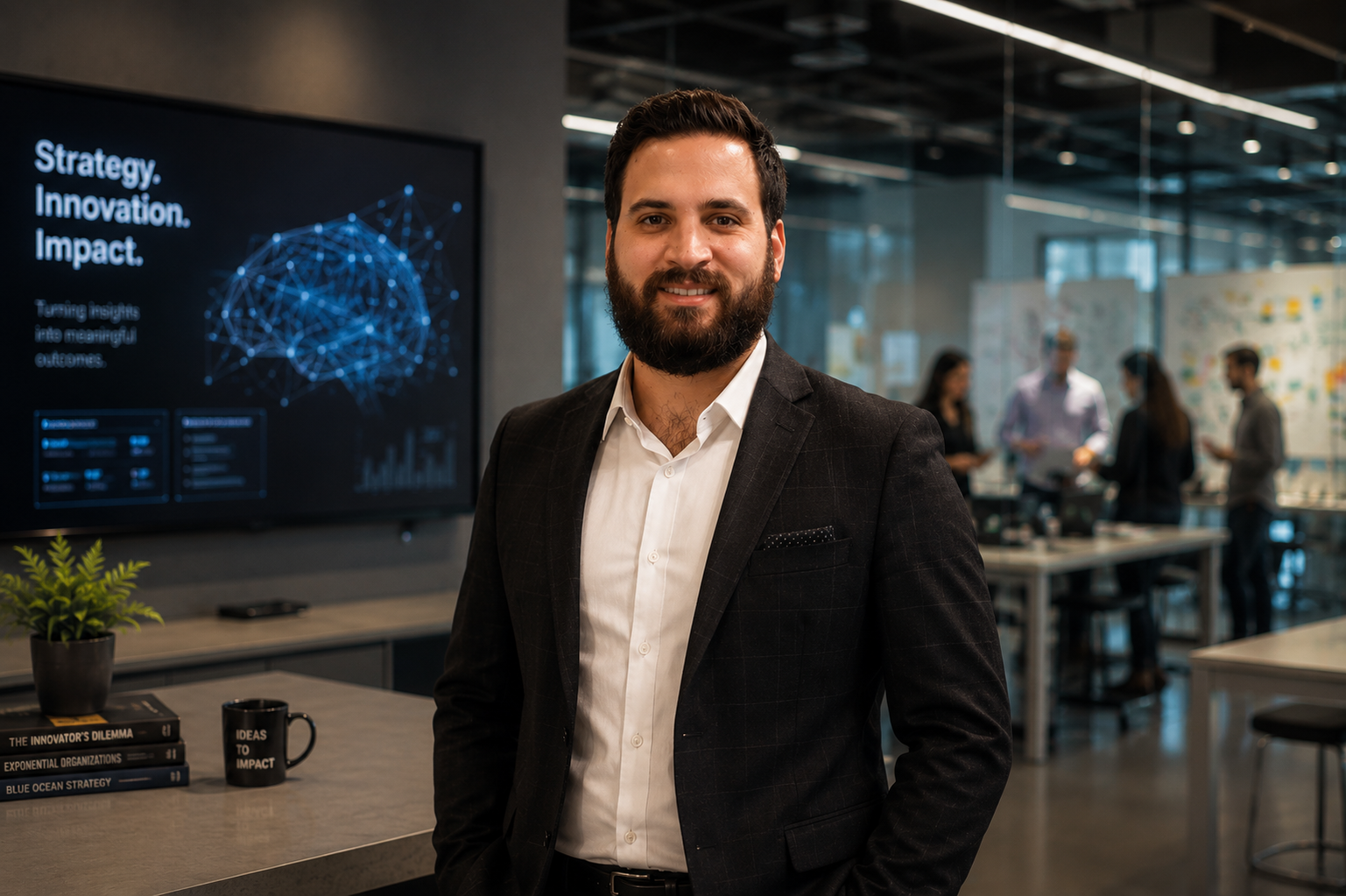 A confident man in a business suit standing in an office or conference room, with a digital presentation display behind him and a group of people working in the background.