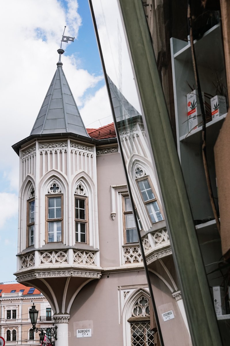 Altstadtgebäude mit Turm und gespiegeltem Turm in Szeged, Ungarn.