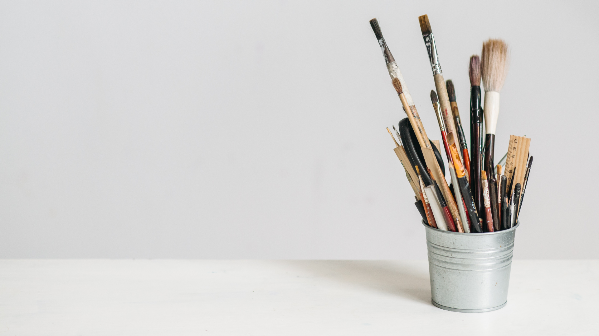Metal container holding assorted paintbrushes and art tools on a white surface.
