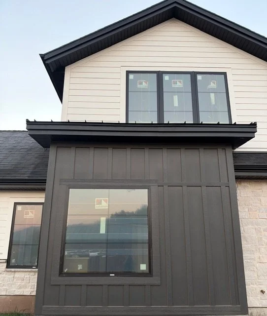 Modern home exterior featuring gray vertical board and batten siding, contrasting dark trim, and decorative window detailing.