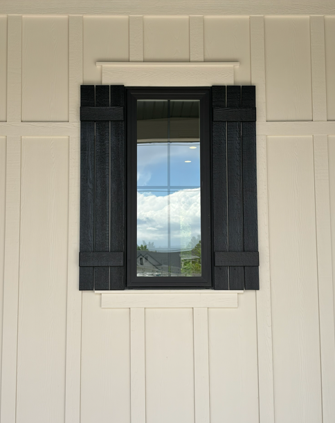 Custom dark-stained wooden window shutters on a home with white board and batten siding