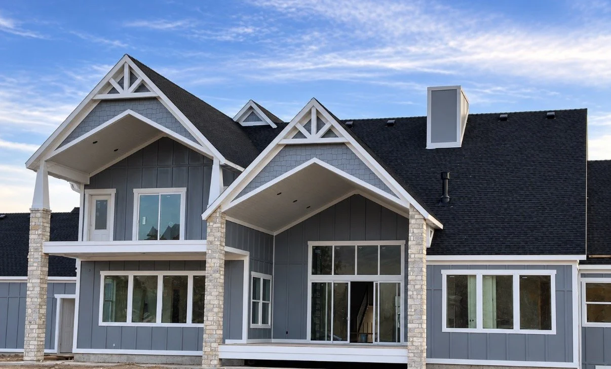 White decorative gable timberwork on a custom home with gray siding and multiple roof peaks