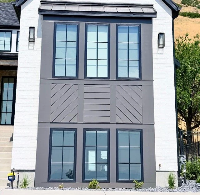 Modern home exterior featuring custom geometric trim panels between upper and lower windows with contrasting architectural details.