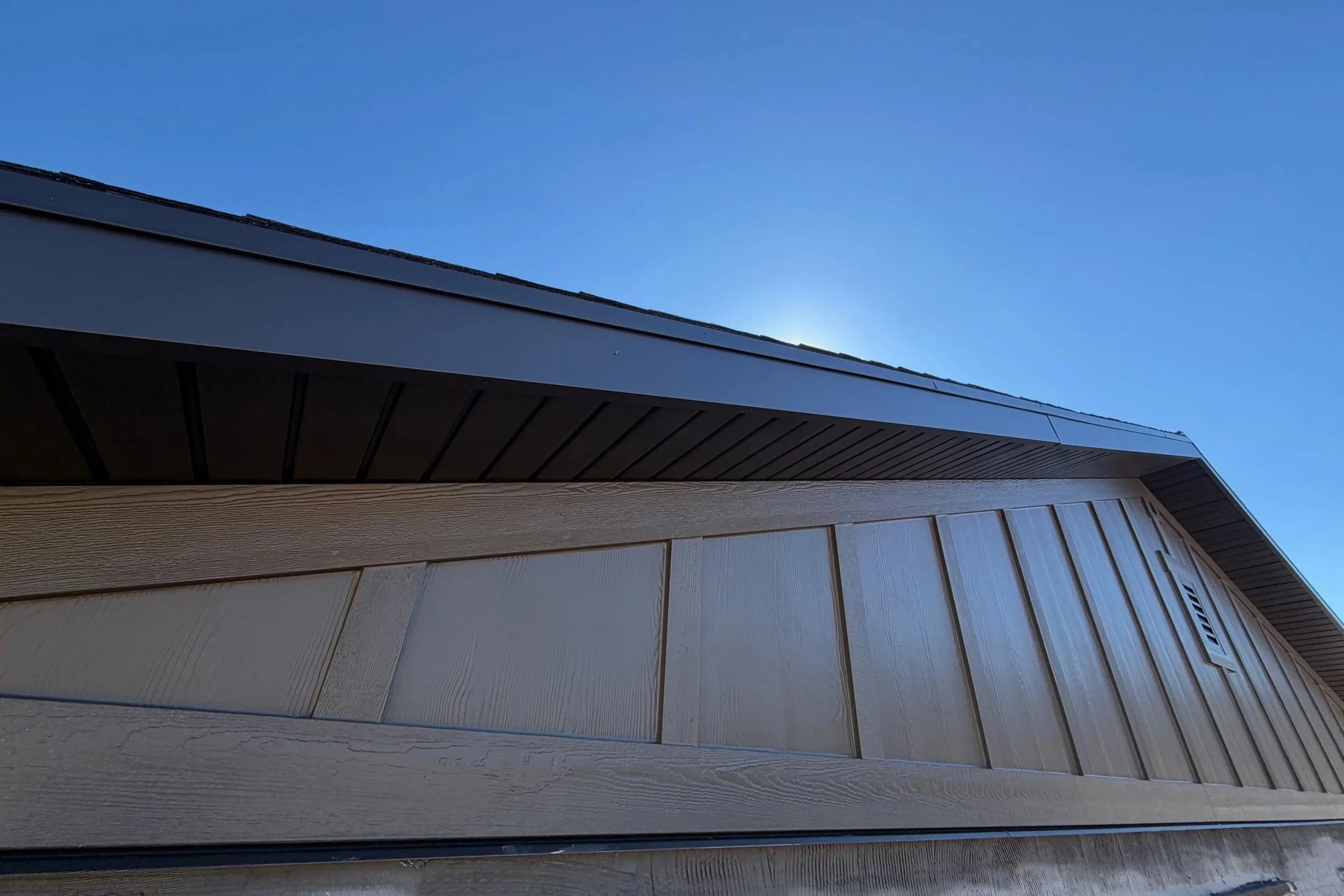 Close-up of dark metal fascia wrapping the roof edge above vertical exterior siding.