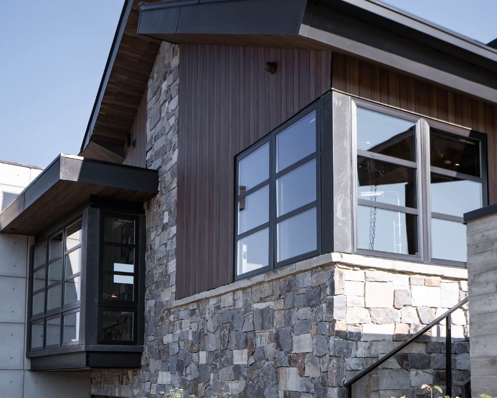 Dark vertical siding paired with light stone masonry and black-framed windows on a contemporary home exterior.