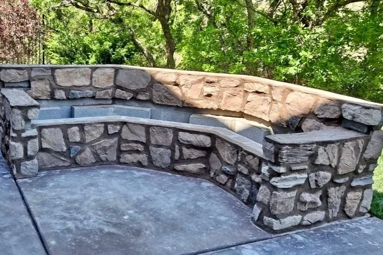 Curved outdoor stone masonry seating wall with a smooth stone cap surrounding a patio area.