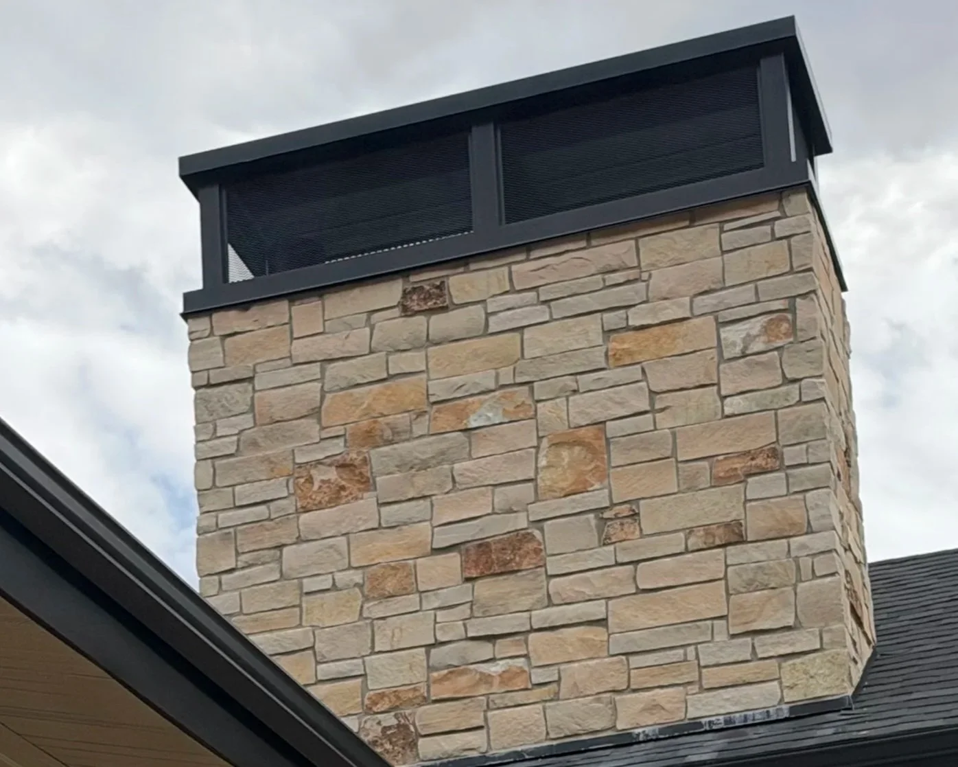Large custom rectangular metal chimney cap with dark vented sides installed on a stone chimney.
