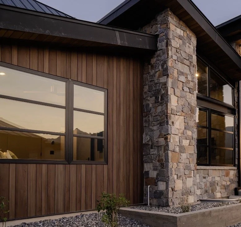 Warm wood-look vertical siding paired with stone masonry columns and large black-framed windows on a modern home.