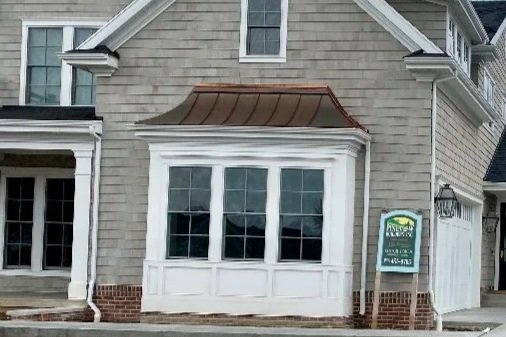 Decorative copper-colored metal overbuild installed above a projecting window on a light-colored home.