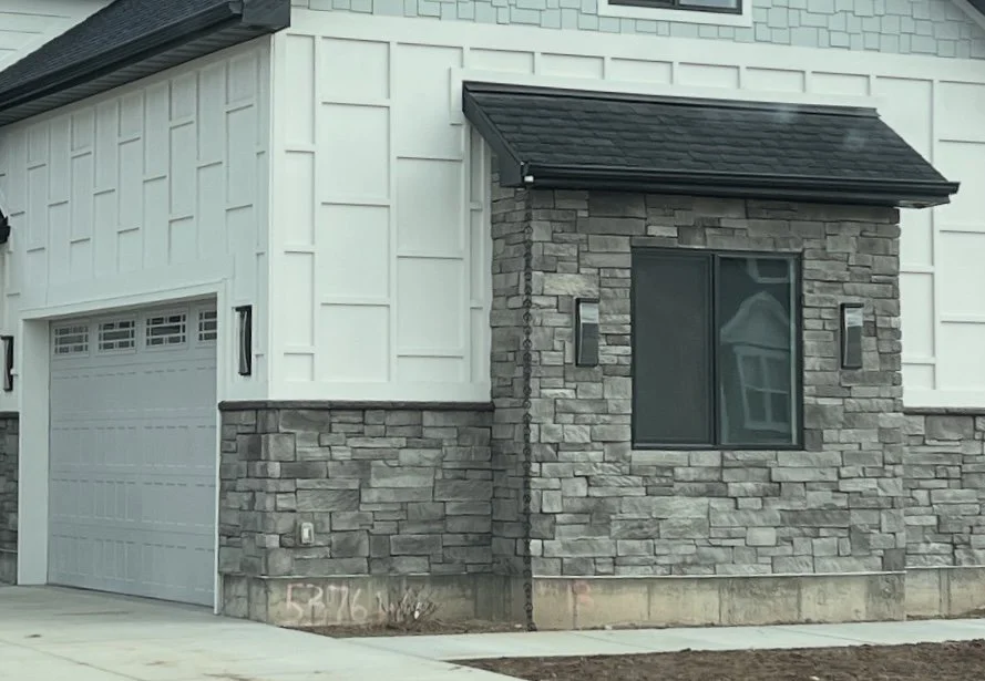White board and batten siding paired with gray stone veneer around a window and garage area.