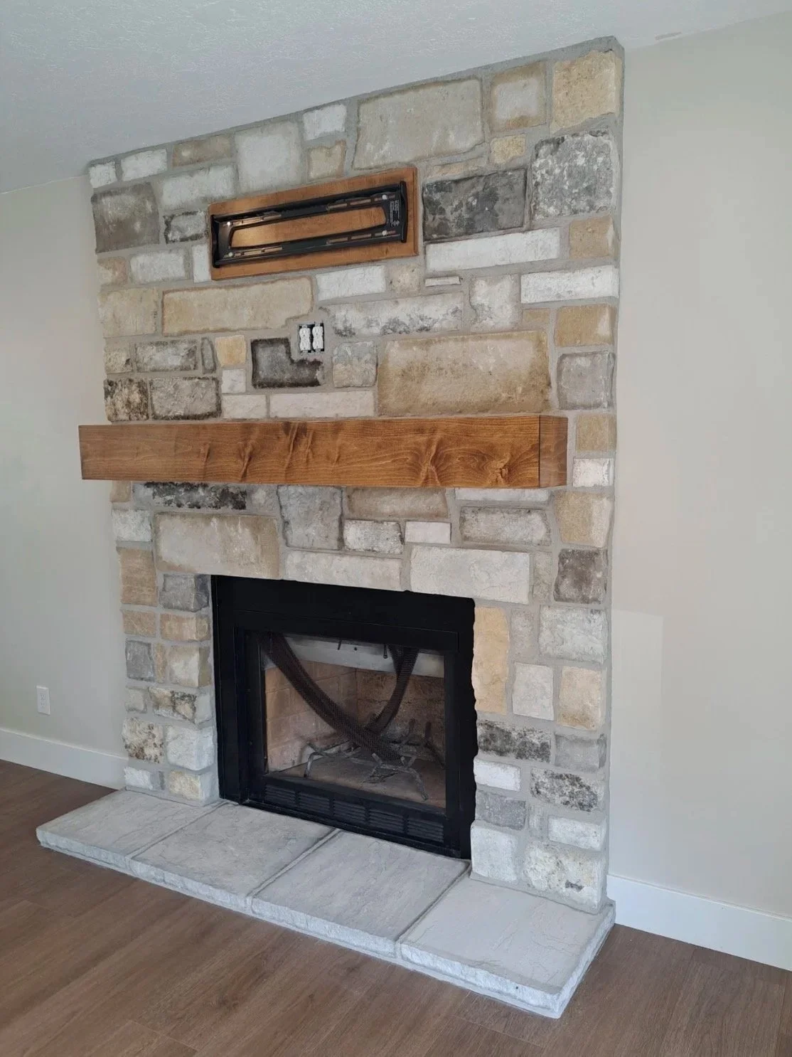 Custom interior stone fireplace with mixed-color stone veneer, a wooden mantel, and a built-in gas fireplace.