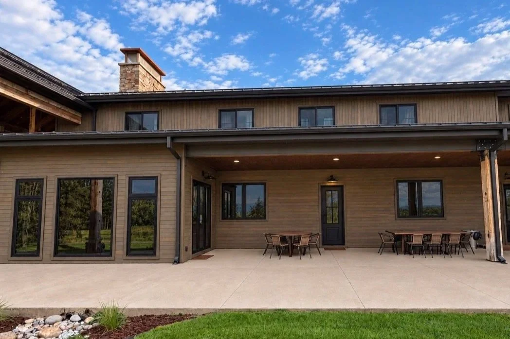 Home exterior featuring warm stained wood siding, timber beams, and a covered patio with natural wood accents.