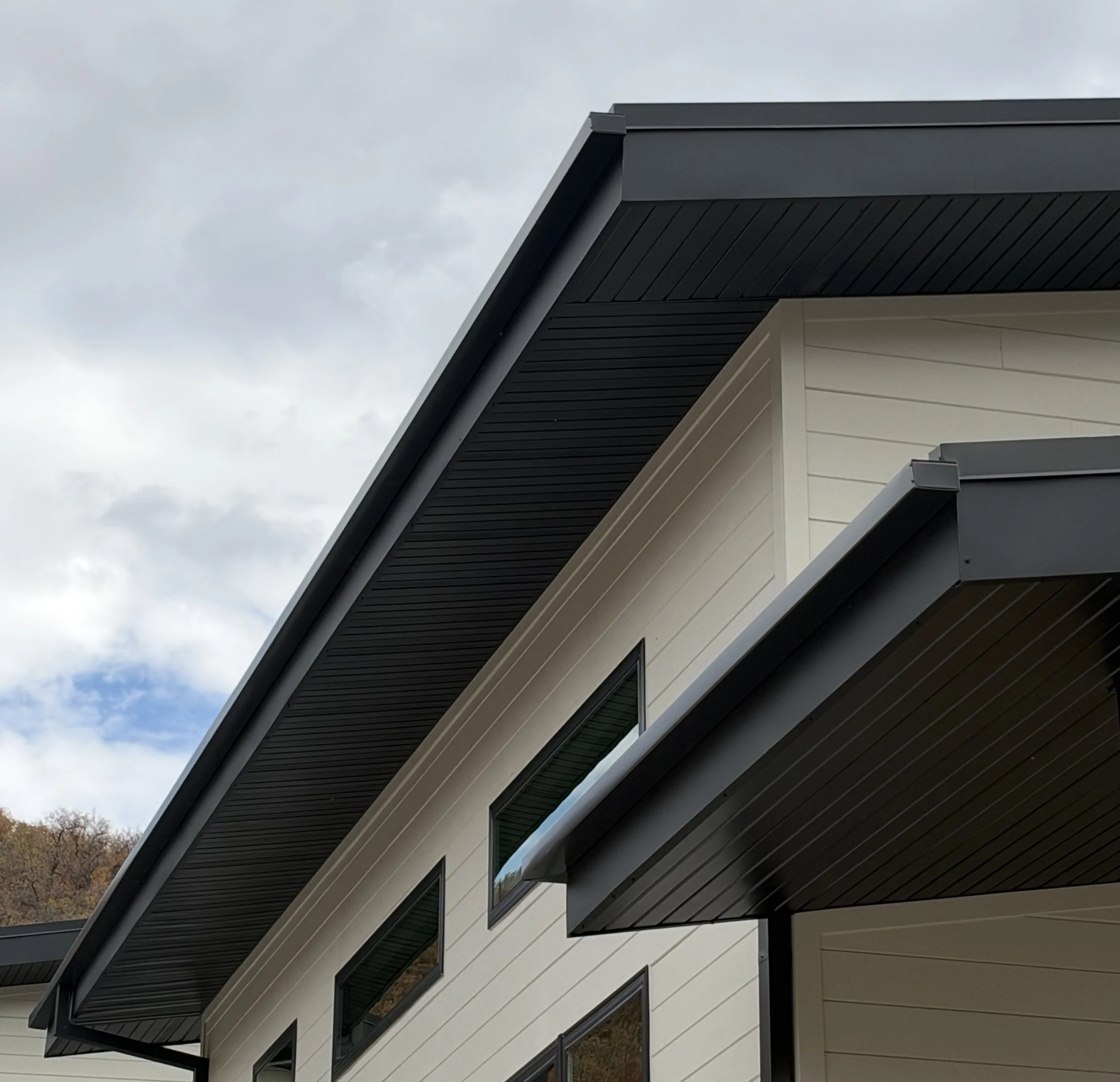 Dark square gutters installed along the roofline of a contemporary home with light-colored siding and black soffit.