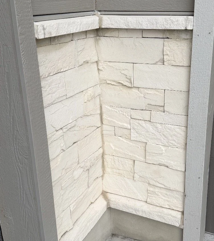 Light-colored manufactured stone veneer installed on an exterior wall beneath white trim