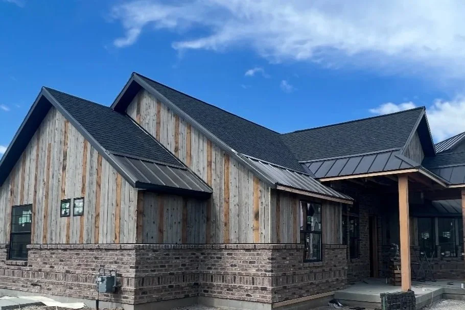 Rustic home exterior with stained wood siding, dark rooflines, and natural stone masonry accents.