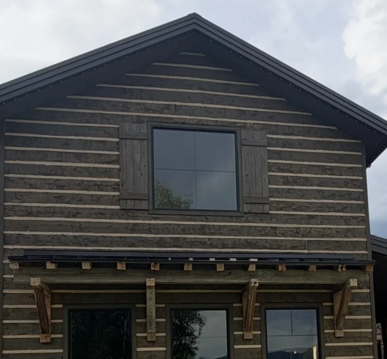 Custom wooden shutters surrounding an upper-story window on a rustic wood-sided home