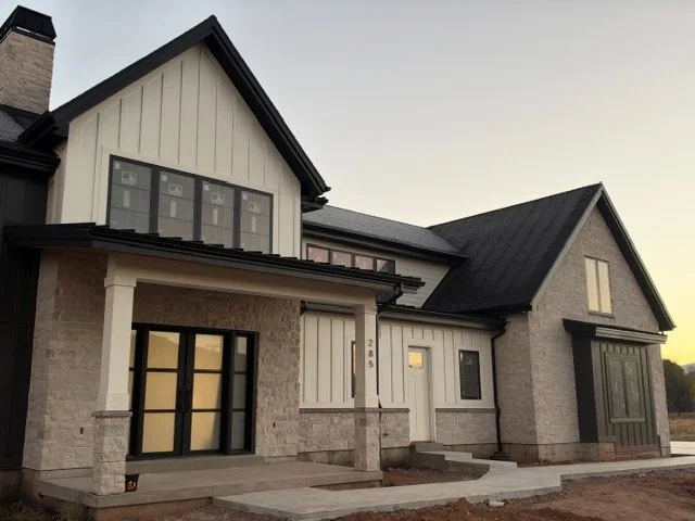 Cream-colored board and batten siding on a custom home with dark rooflines, timber accents, and stone masonry.