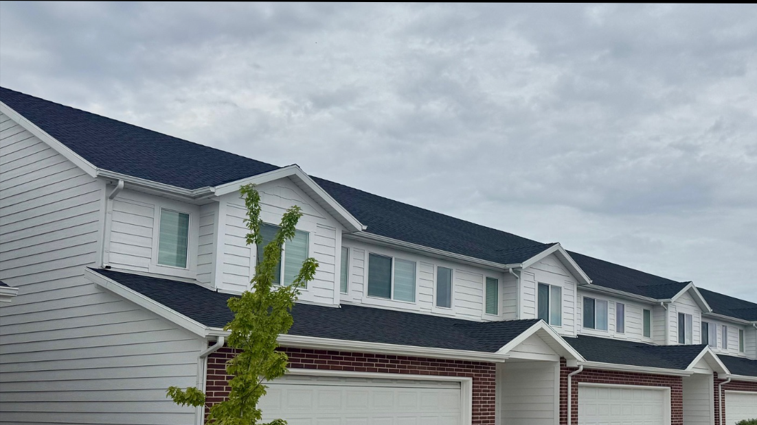 Large two-story home featuring light-colored horizontal lap siding, white exterior trim, and multiple garage doors.