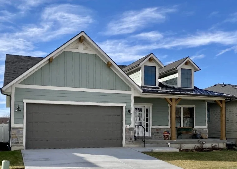 Custom home exterior featuring light blue vertical siding, white window and garage door trim, and decorative gable accents.