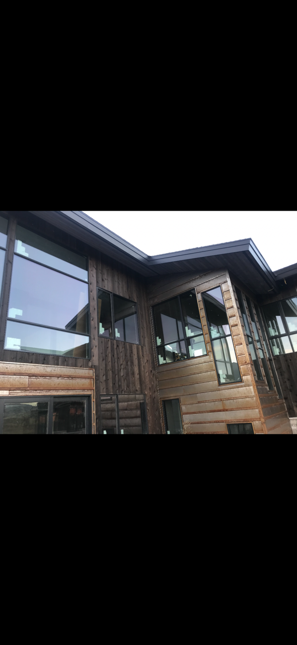 Rustic custom home exterior featuring stained wood siding, natural stone masonry, custom window trim, soffit, fascia, and architectural details.
