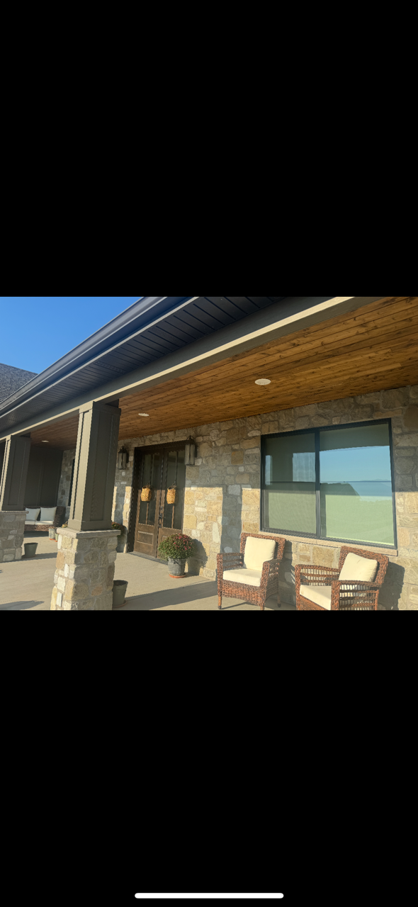 Custom home exterior with natural stone masonry, stained cedar porch ceiling, columns, soffit, fascia, and exterior trim by Huff's Siding.