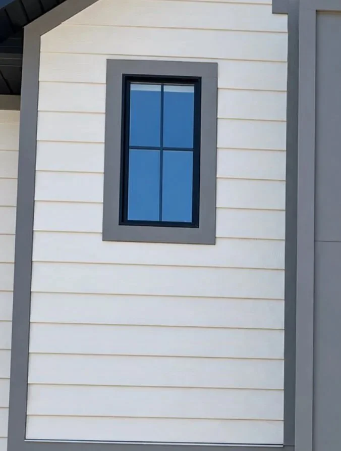 Close-up of light-colored horizontal lap siding surrounding a black-framed window with contrasting exterior trim.
