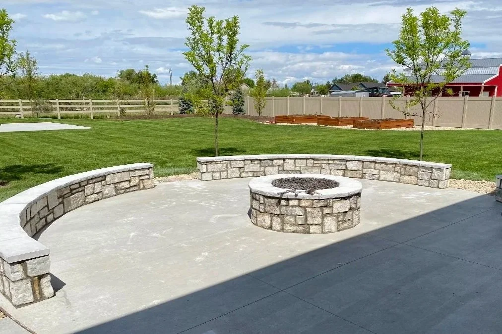 Outdoor stone masonry seating wall surrounding a circular fire pit in a landscaped backyard patio.