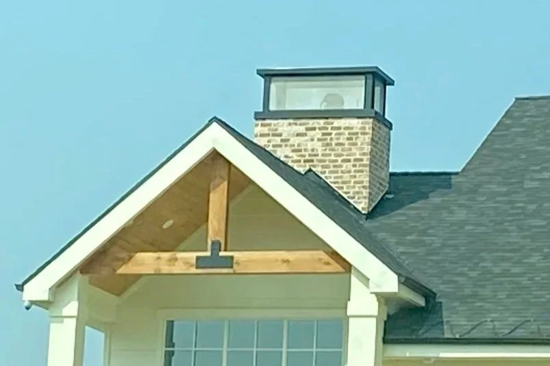 Light-colored fascia outlining a decorative front gable beside a stone chimney.
