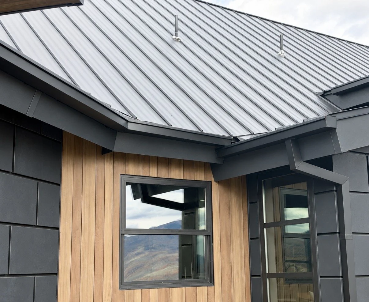 Gray square gutters installed beneath a standing-seam metal roof on a modern home with wood and gray siding.
