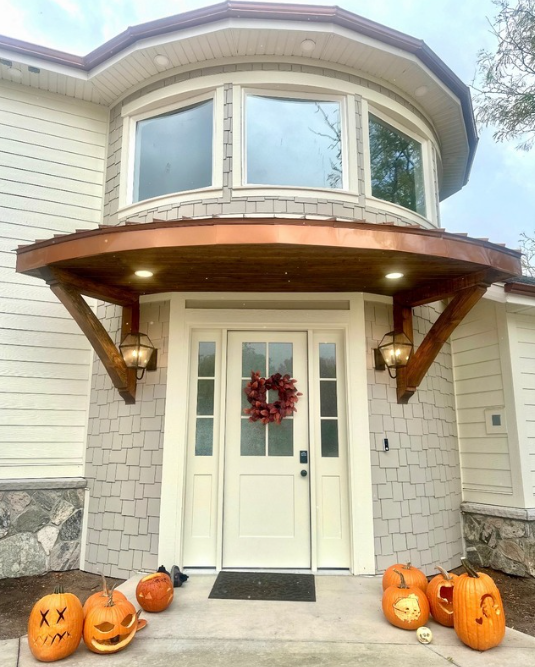 Decorative shake-style siding surrounding a curved second-story window and front entrance with white trim and timber accents.