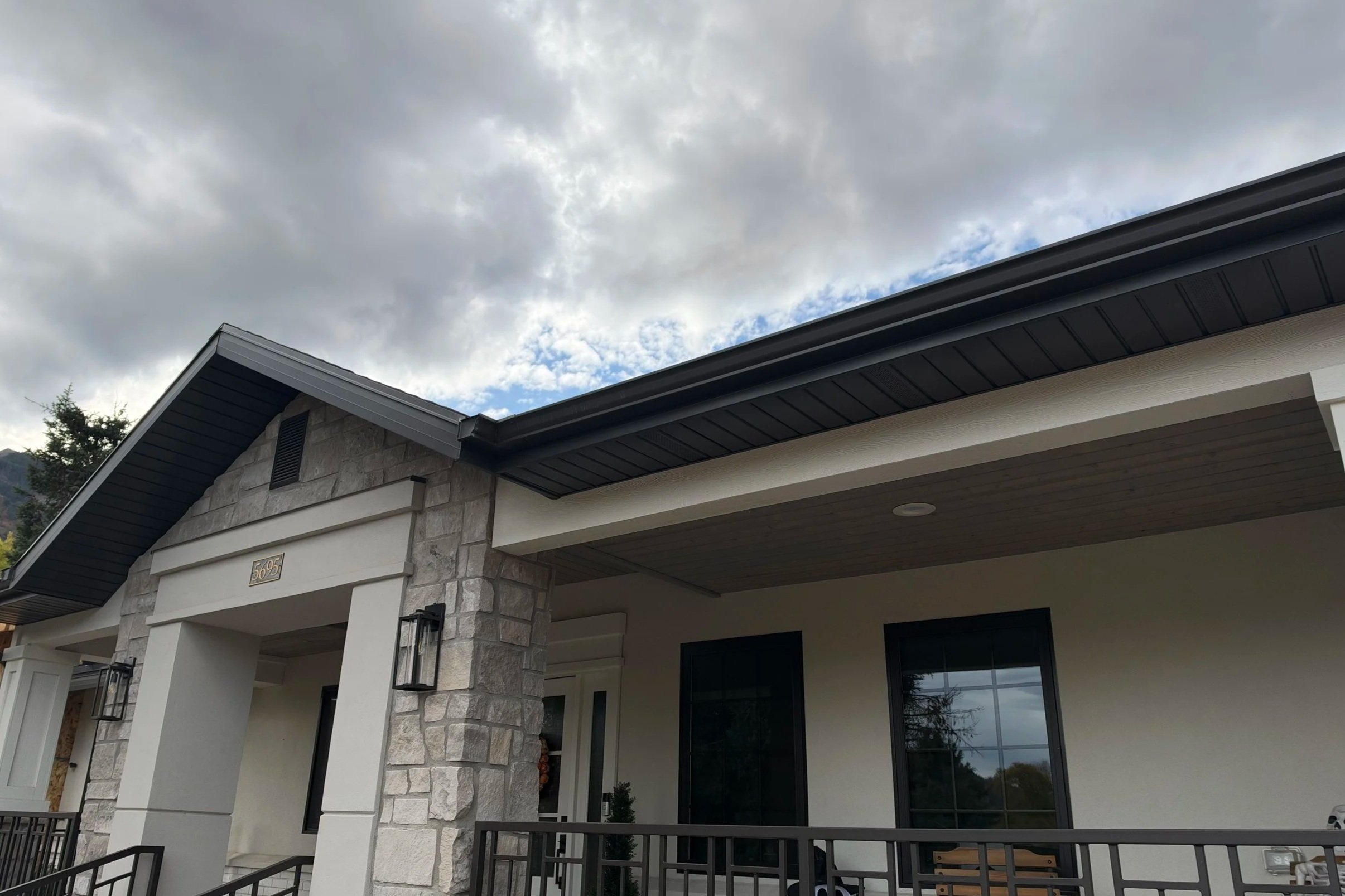 Black K-style gutters installed along the roofline of a white home with stone accents and matching black soffit and fascia.