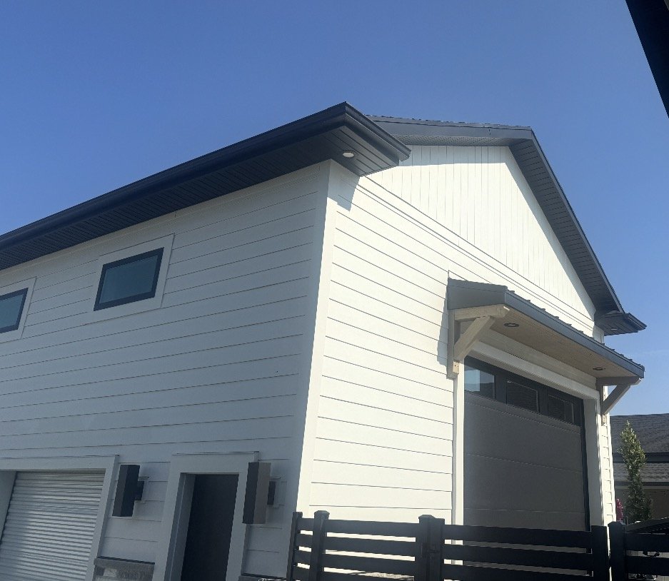 White horizontal lap siding installed on a two-story shop building with dark roof trim and large garage openings.