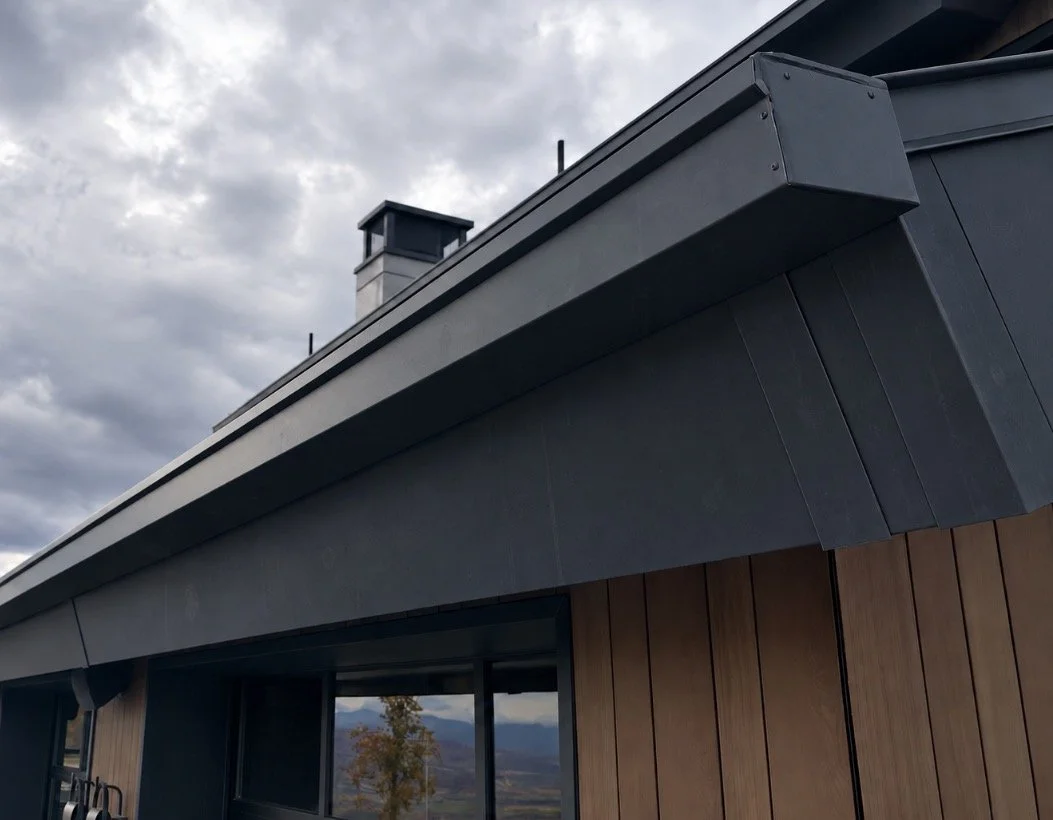 Square-profile metal gutter installed along a modern roofline with dark siding and natural wood exterior accents.