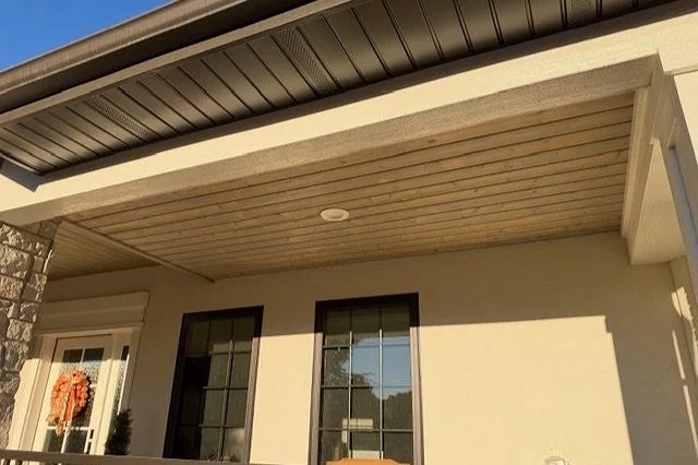 Finished tongue-and-groove porch ceiling with a light wood-tone finish, recessed lighting, and white exterior trim.