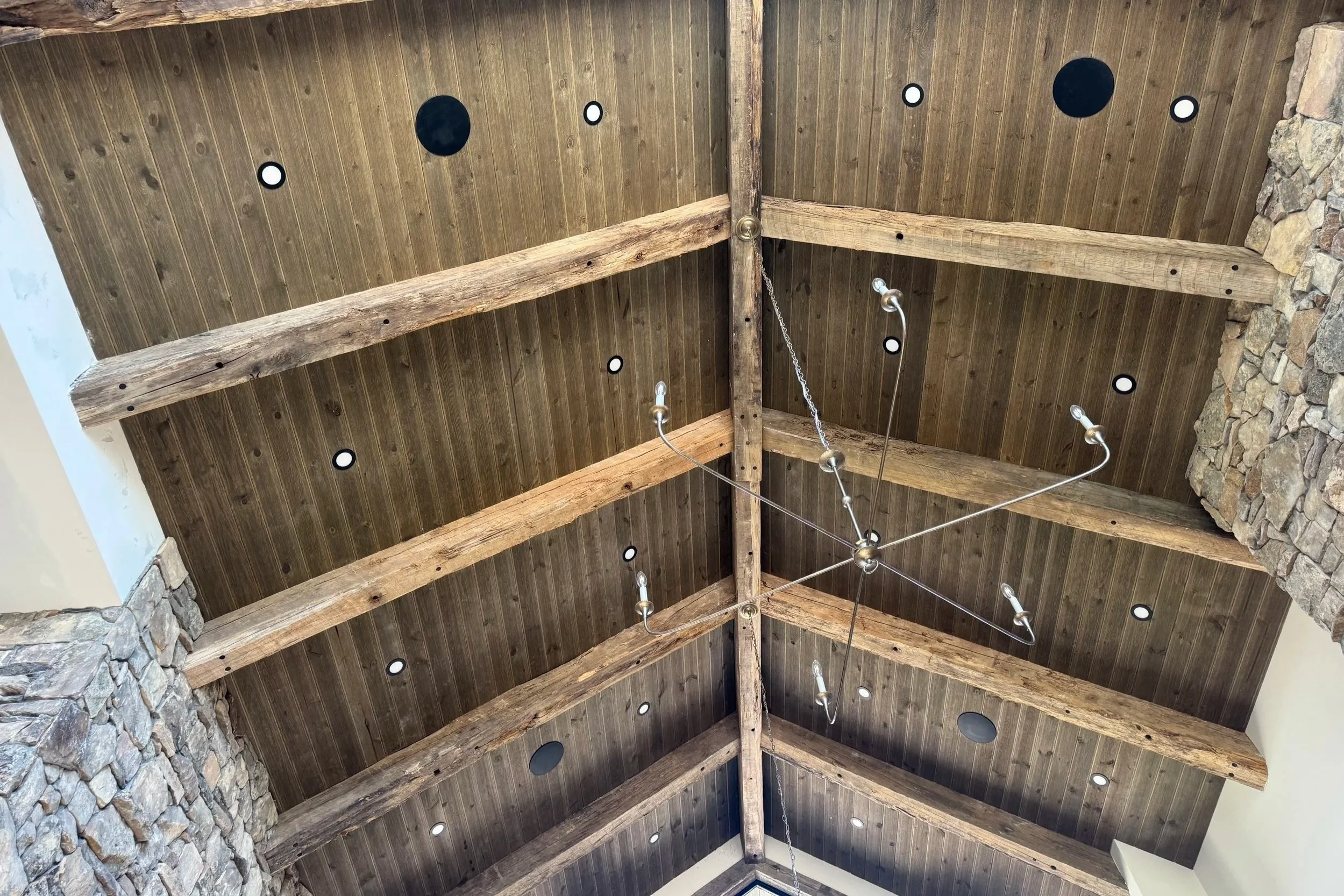 Stained tongue-and-groove wood ceiling with exposed timber beams and recessed lighting beneath a covered roof.