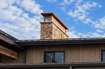 Custom stone masonry chimney extending above the roofline of a home with natural wood siding and dark roofing.