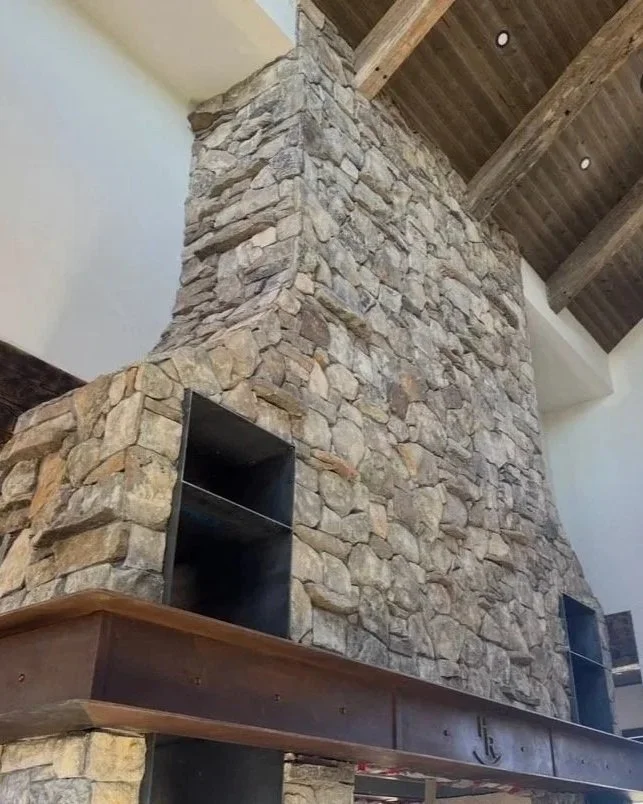 Tall stone masonry fireplace and chimney with a recessed firebox beneath a covered outdoor roof structure.
