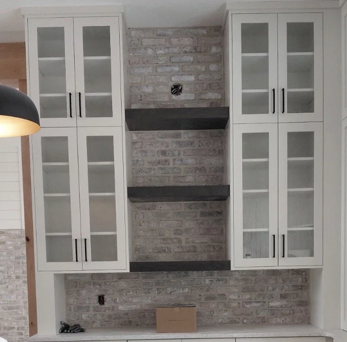 Thin brick kitchen backsplash with floating wood shelves between white cabinets