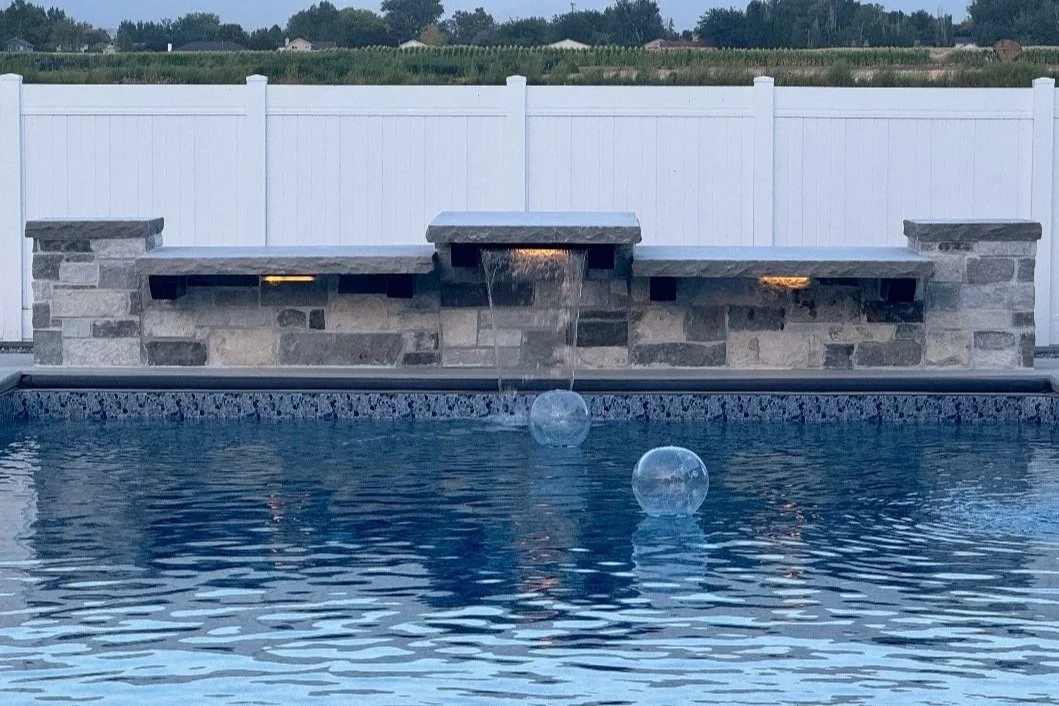 Custom stone masonry pool feature with a raised waterfall and decorative stone wall along the swimming pool.