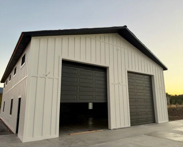 Large detached garage featuring white board and batten siding, dark garage doors, and contrasting exterior trim.