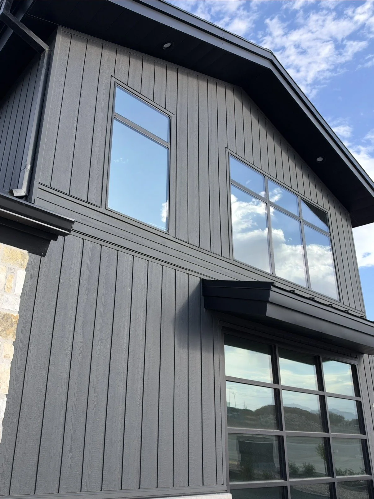 Light-colored vertical siding on a modern two-story exterior with dark trim and large windows.