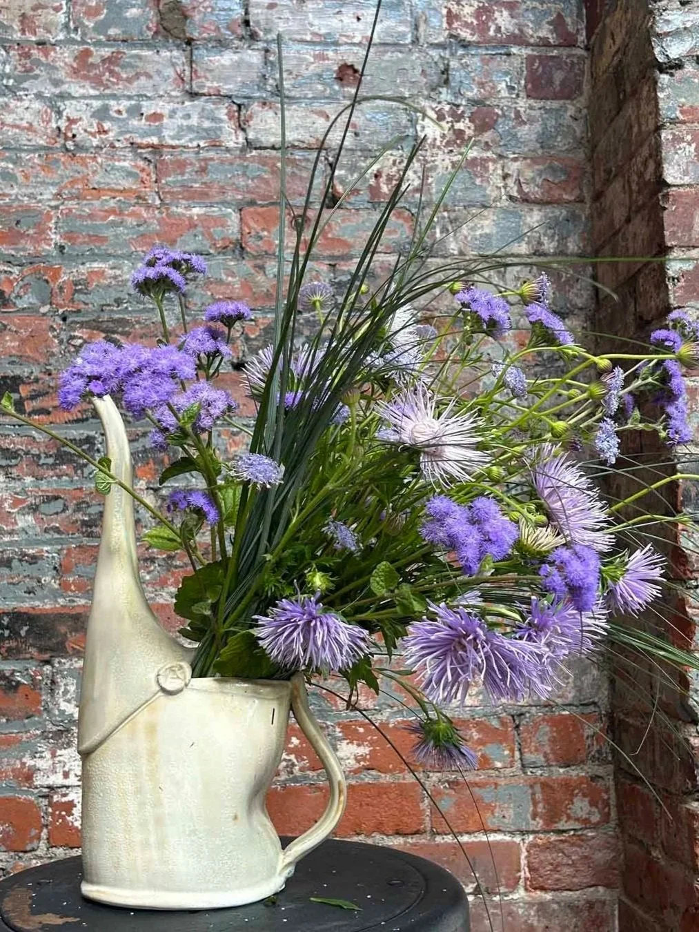 brown watering cn in front of brick wall with purple flowers