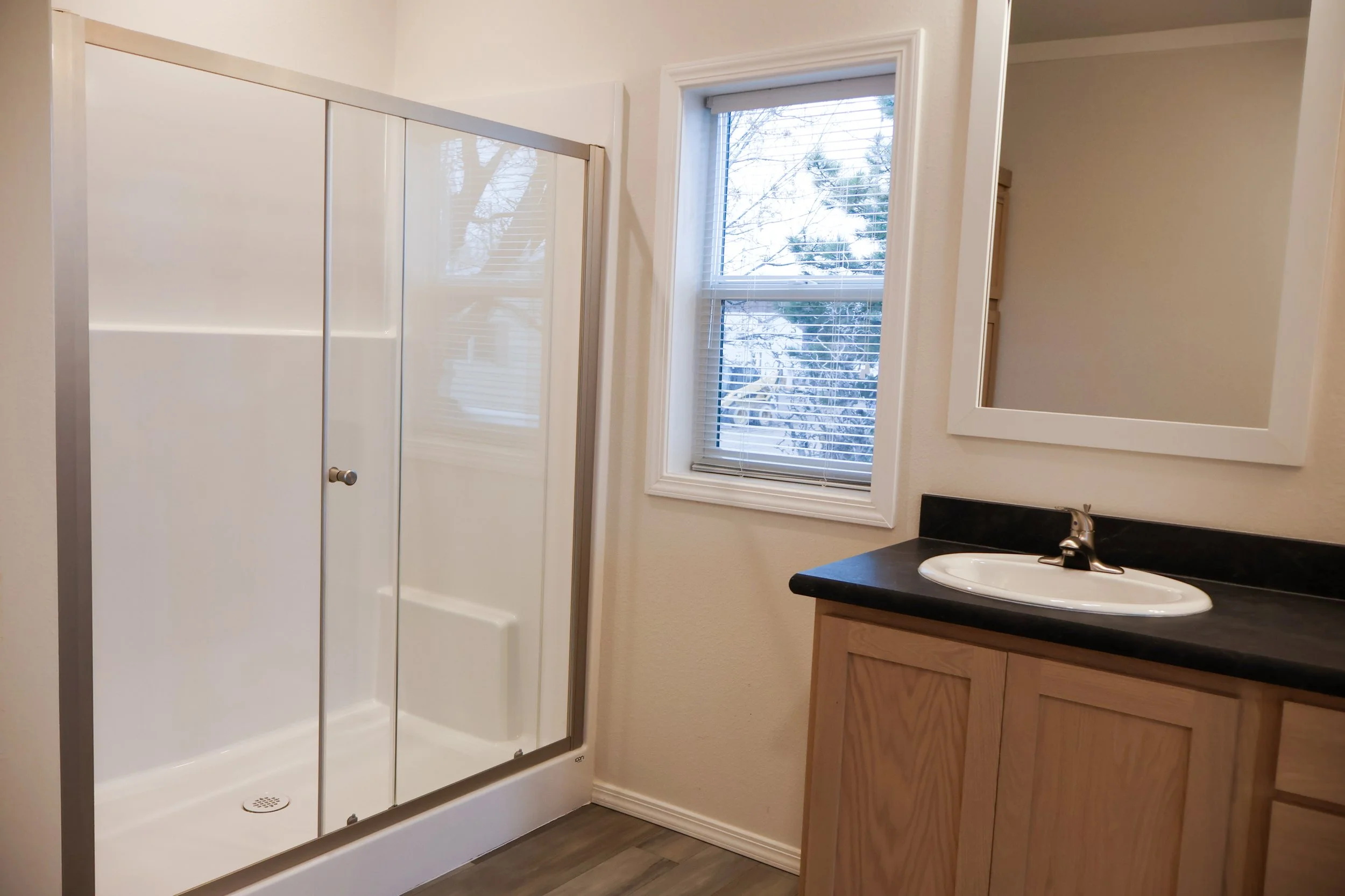 Bathroom with a shower, a window with blinds, a mirror, a sink, and a wooden cabinet.
