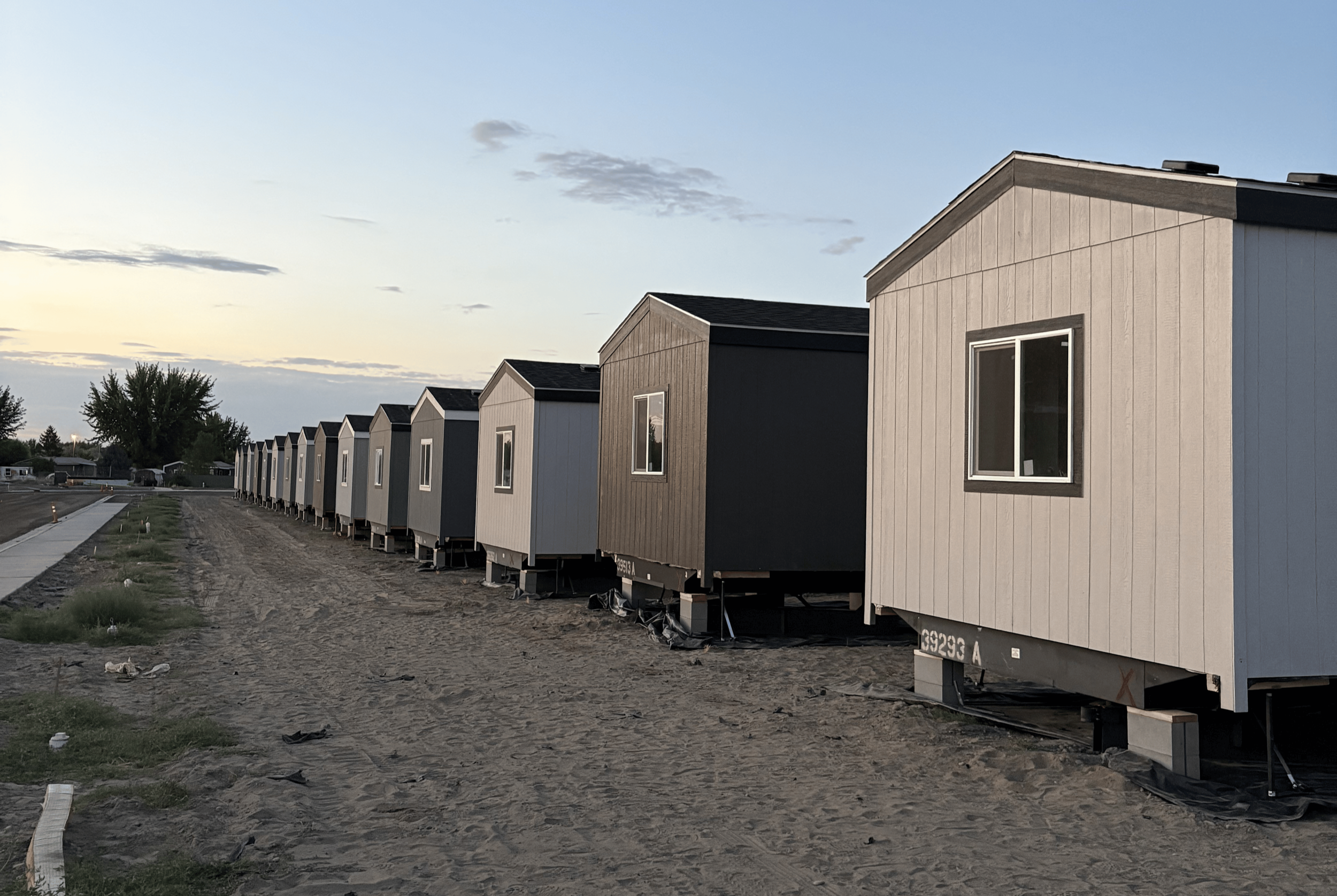Multiple new tiny house trailers lined up on a dirt lot during sunset.