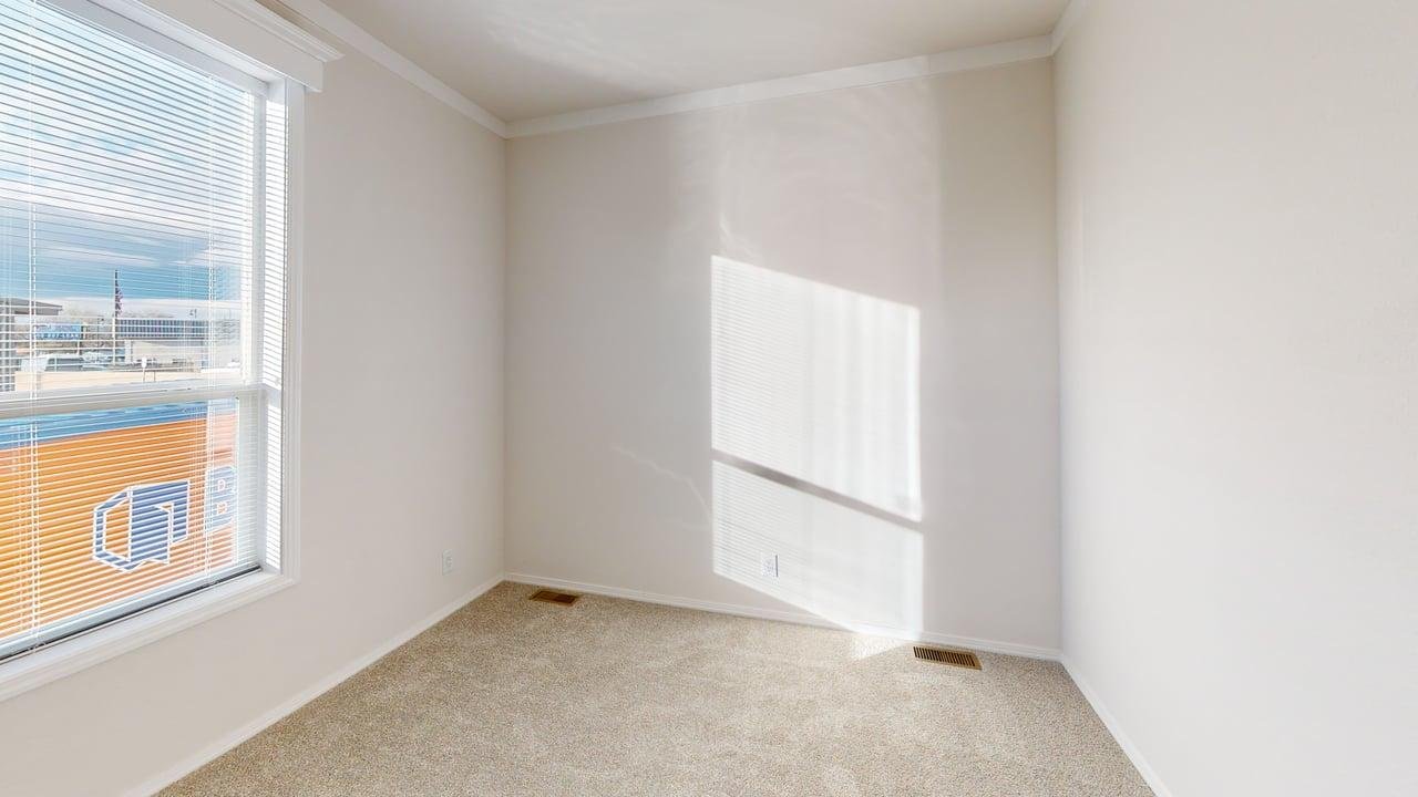 Empty room with white walls, beige carpet, and a window with closed blinds letting in sunlight.